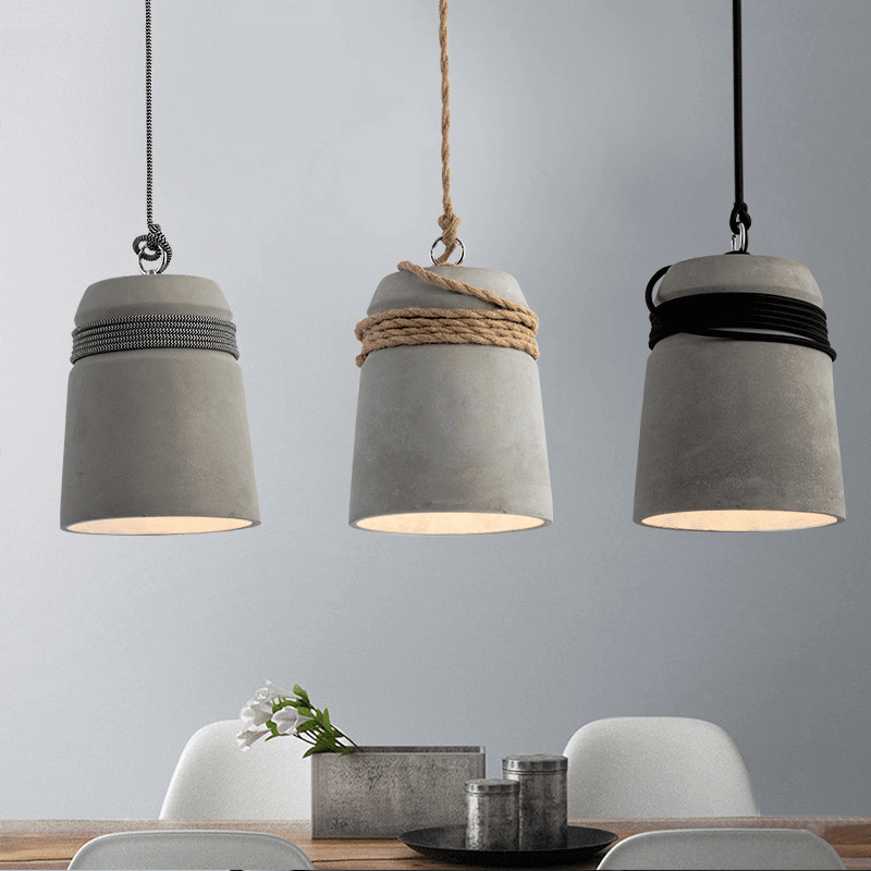 Concrete pendant light fixtures with hemp rope hanging above a dining table, showcasing a minimalist and industrial design.